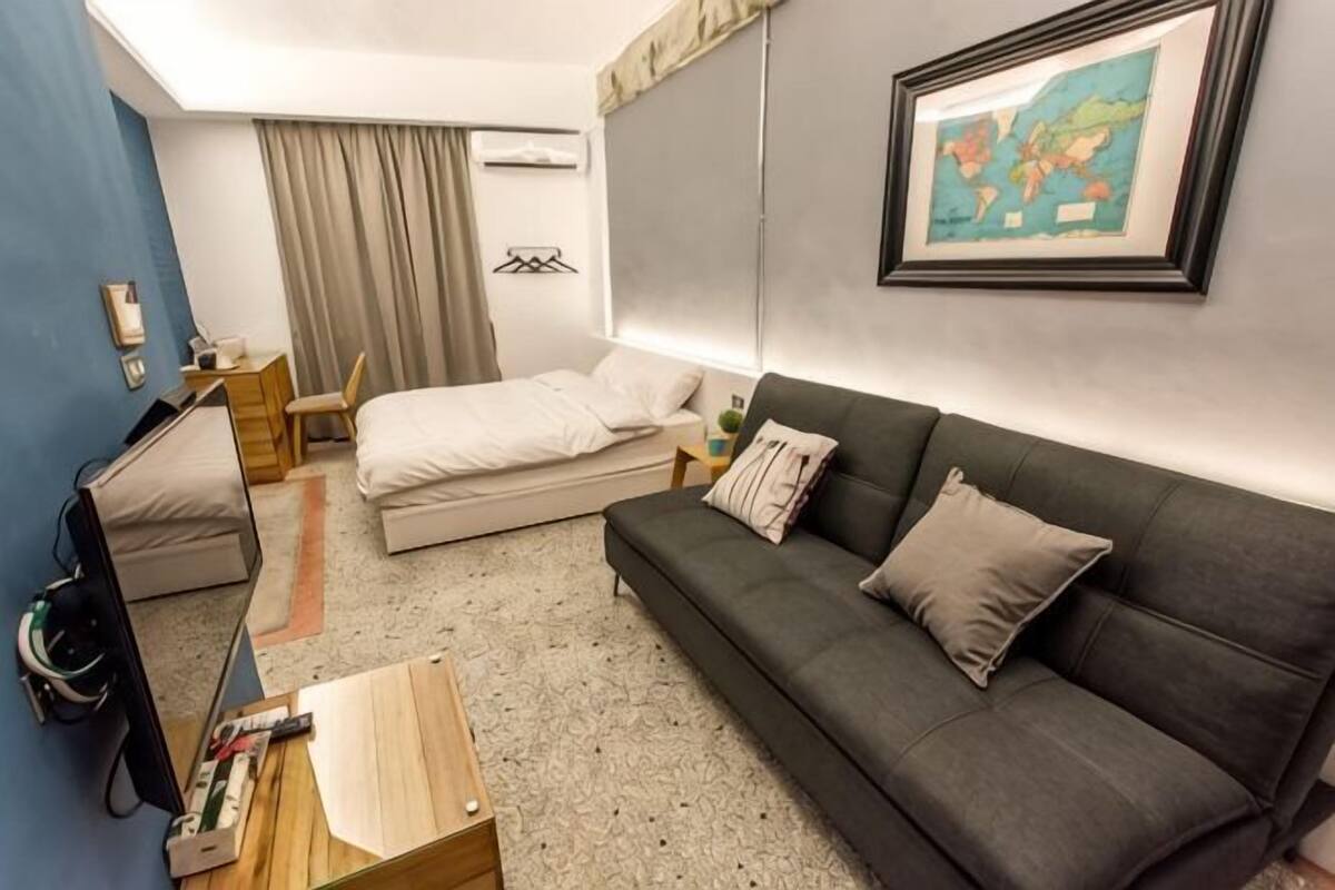 A hotel room with a bed, a sofa, a desk, a chair, and a TV.