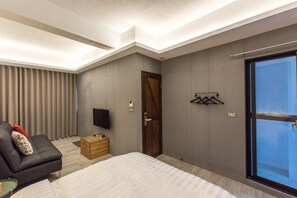 A modern hotel room with a large bed, a sofa, a TV, and a sliding glass door to the outside. - Blue House (Tainan)