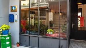 Una entrada de edificio con un gran ventanal, un buzón azul y un barril verde.