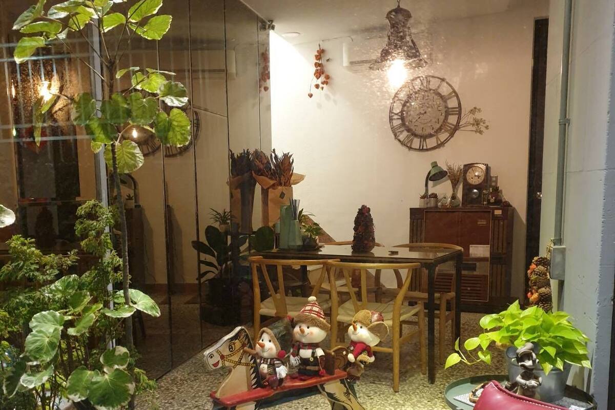 A cozy living room with a red leather sofa, a wooden coffee table, and a small table with decorative items. There are potted plants and a hanging light fixture.
