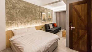 Un dormitorio moderno con una cama grande, un sofá oscuro y una puerta de madera.