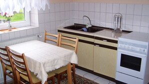 Una cocina con un lavamanos, estufa y sillas de madera alrededor de una mesa.