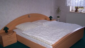 Una cama individual con cabecera de madera, una mesita de noche con lámpara y una ventana con cortinas de encaje.
