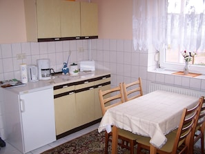 A kitchen with a dining table, chairs, a coffee maker, a toaster, and a window with curtains. - Fewo Tannenhof EC - Fewo Tannenhof (Dahmen)