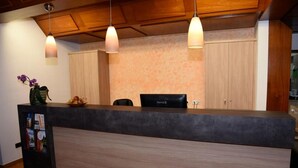 A reception desk with a black counter, wooden cabinets, and pendant lights. - Hotel Weisses Lamm (Allersberg)