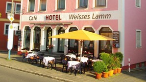 A pink building with "HOTEL" and "Weisses Lamm" signage, featuring outdoor seating and a café. - Hotel Weisses Lamm (Allersberg)