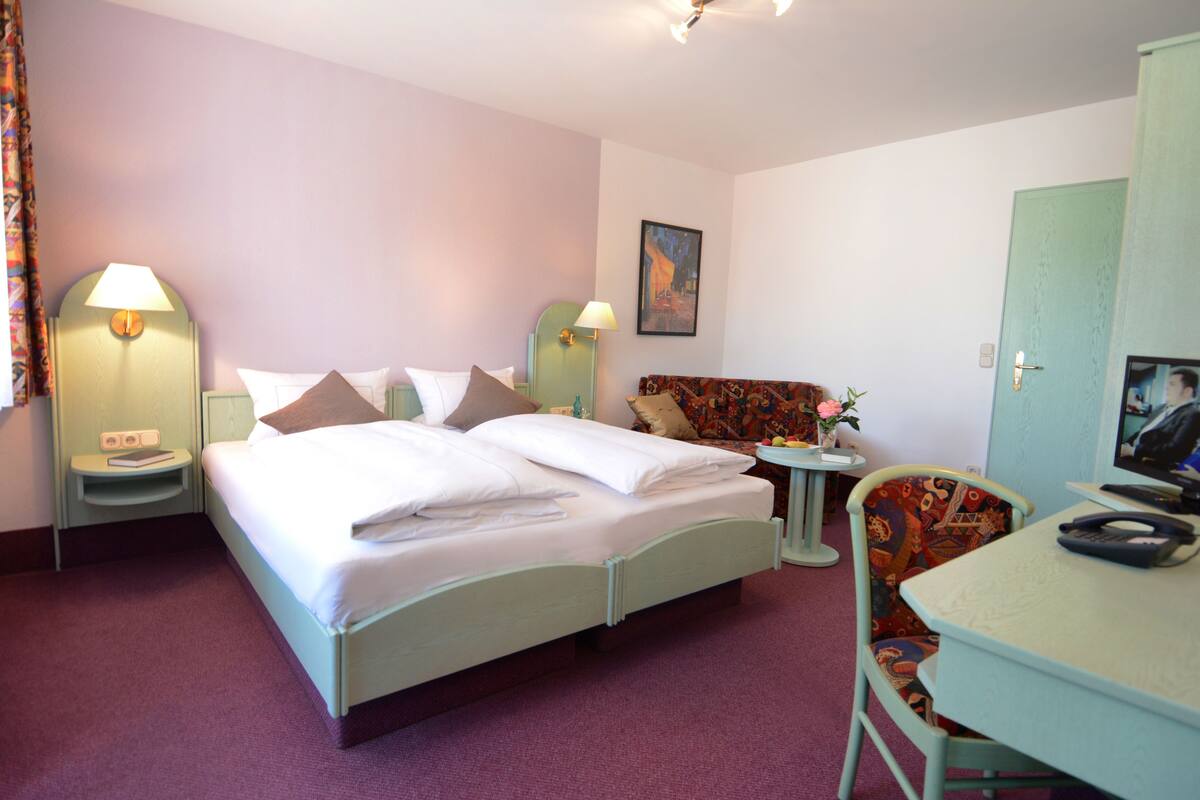 A hotel room with a bed, bedside tables, a chair, a desk, and a television.