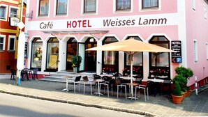 A pink building with the sign "HOTEL Weisses Lamm" and outdoor seating with umbrellas. - Hotel Weisses Lamm (Allersberg)