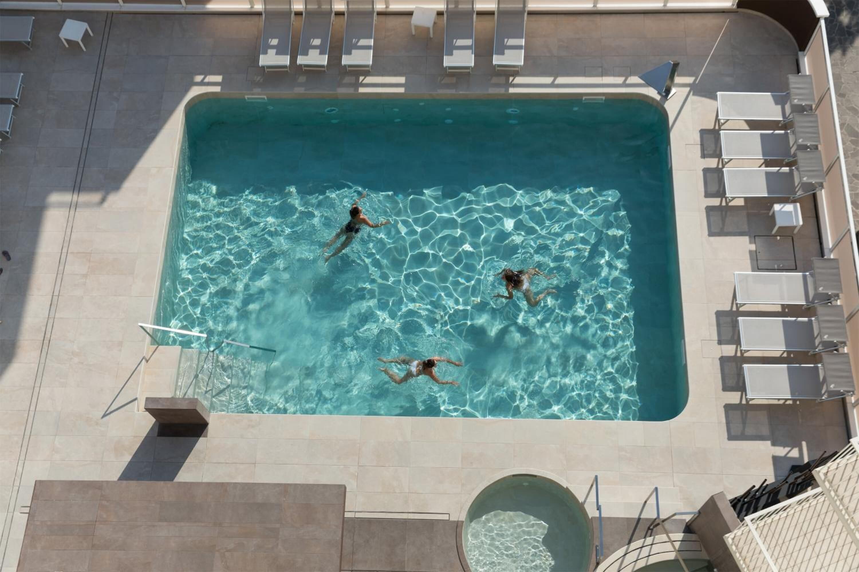 A rectangular swimming pool with clear water, surrounded by lounge chairs and a tiled deck.