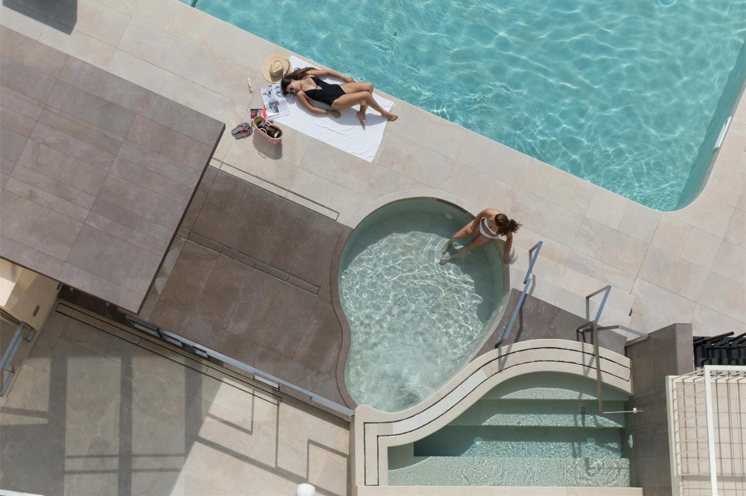 A swimming pool with a sunbed and lounge chair, a small pool area, and a poolside area with a tiled deck.