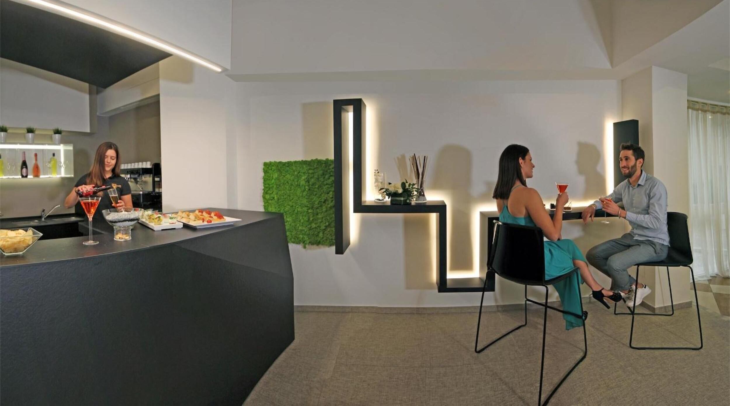 A modern hotel lobby with a reception desk, a green wall, and a seating area with two chairs.