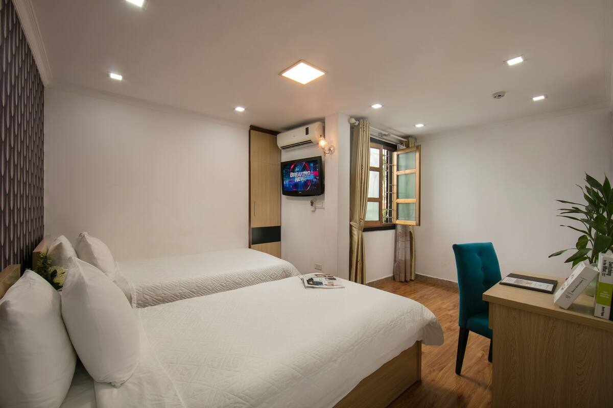A hotel room with two beds, a desk, a TV, and a window.
