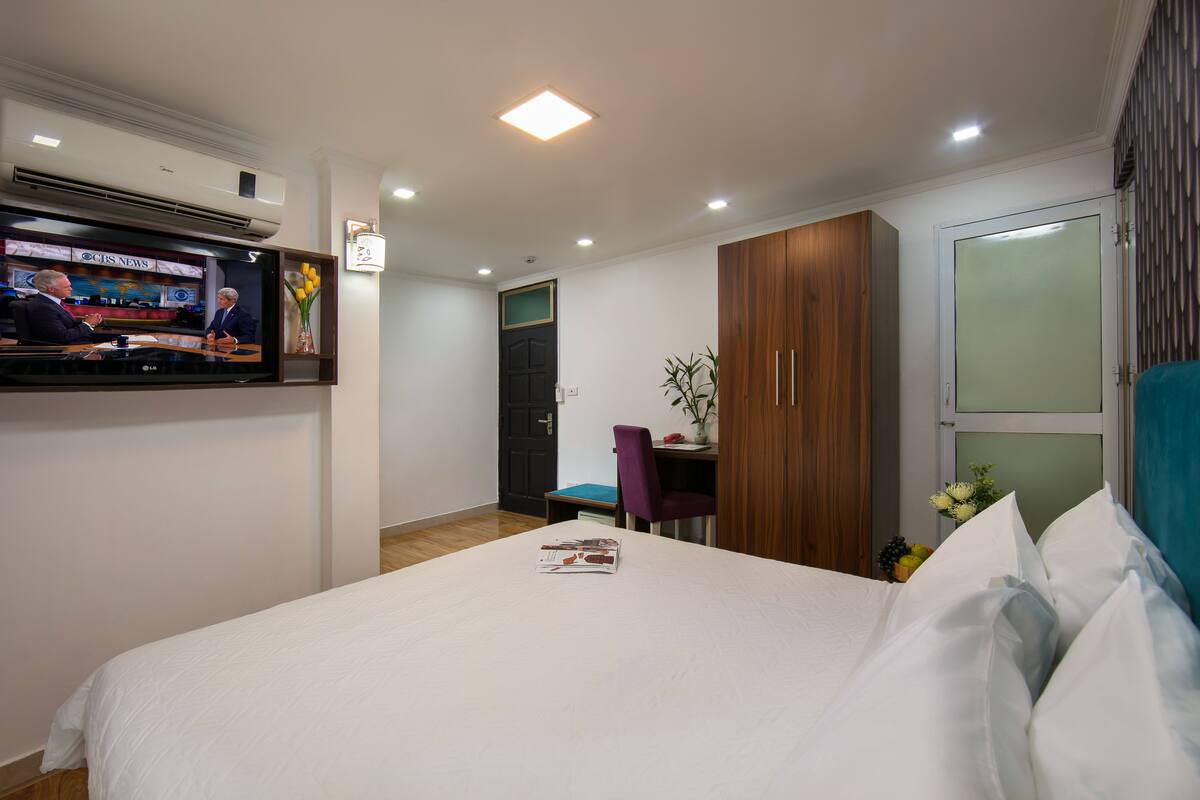A hotel room with a bed, a desk, a television, and a wardrobe.