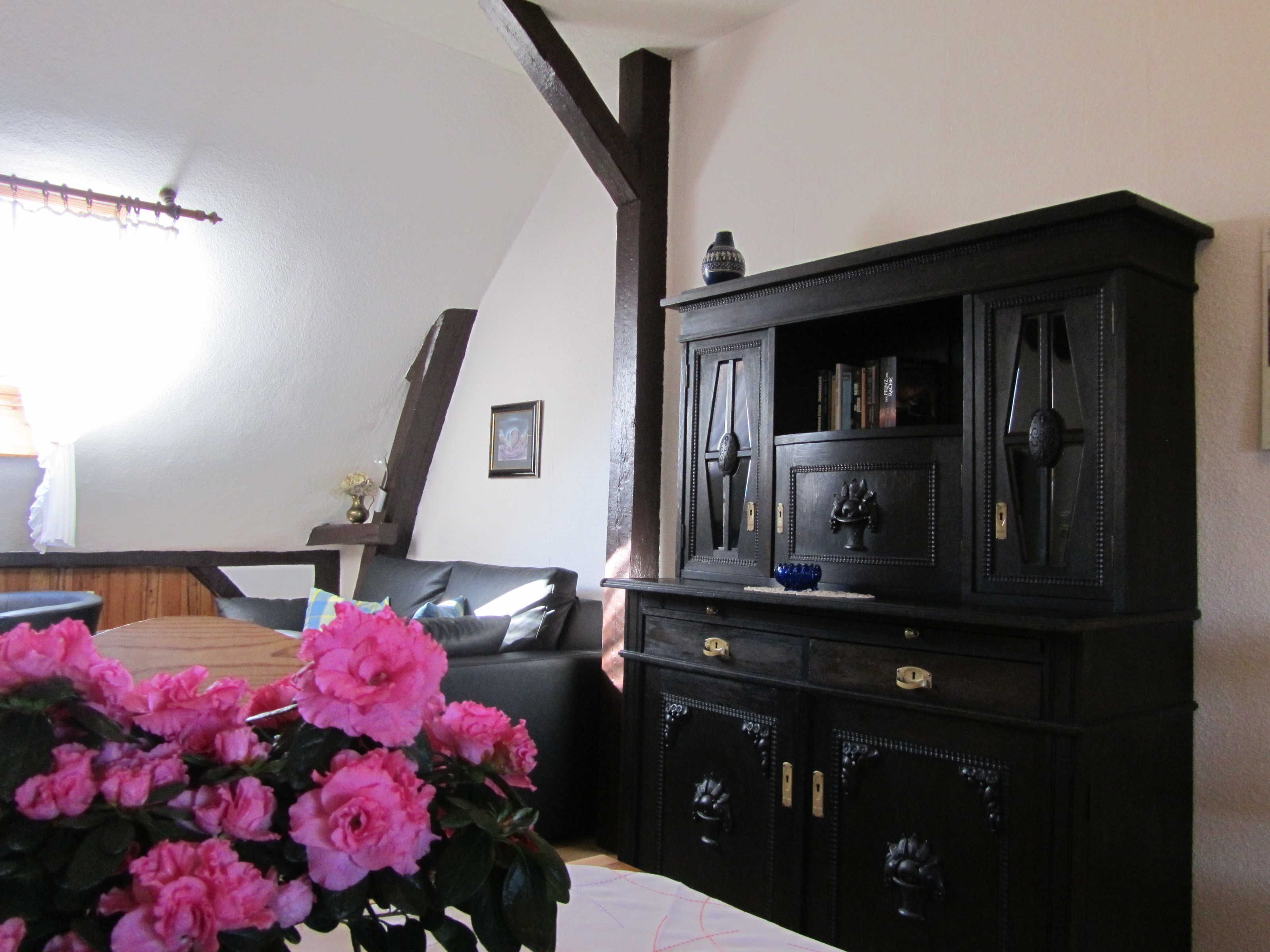 Ein Wohnzimmer mit einem dunklen Holzschrank, einer Couch und einer Vase mit rosa Blumen.