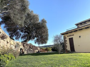 Un muro de piedra, un árbol grande y un edificio con tejado de baldosas.