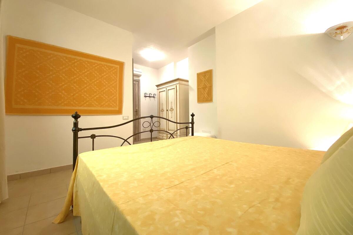 Quarto com cama, guarda-roupa e porta que dá para outro espaço.