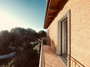 Un balcón con suelo de baldosas, baranda de madera y vistas a árboles y una ladera.