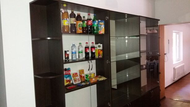 A dark-colored cabinet with multiple shelves containing various beverages and snacks. - Nursat Guest House (Astana)