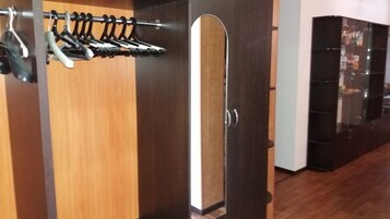 Un armario de madera con espejo, un perchero con perchas y una puerta oscura.