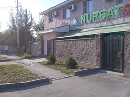 A building with a sign reading "NURSAT" and a stone wall.