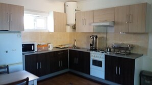 A kitchen with dark cabinets, a stove, a microwave, and a coffee maker. - Nursat Guest House (Astana)