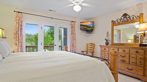 A bedroom with a large bed, a dresser, a chair, a television, and a balcony with curtains. - Evergreens 1022- Mtn Condo, Gated Resort, Indoor/Outdoor Pools & Hot Tub (Boone)