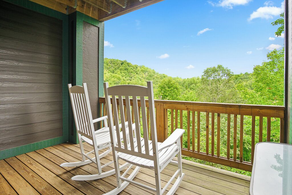 Una terraza de madera con dos mecedoras y vistas a un paisaje boscoso.