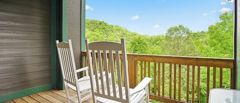 Una terraza de madera con dos mecedoras y vistas a un paisaje boscoso.