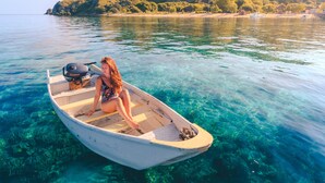 Un bateau sur lequel se trouve une personne, naviguant sur une étendue d’eau claire, entouré de verdure et de collines.