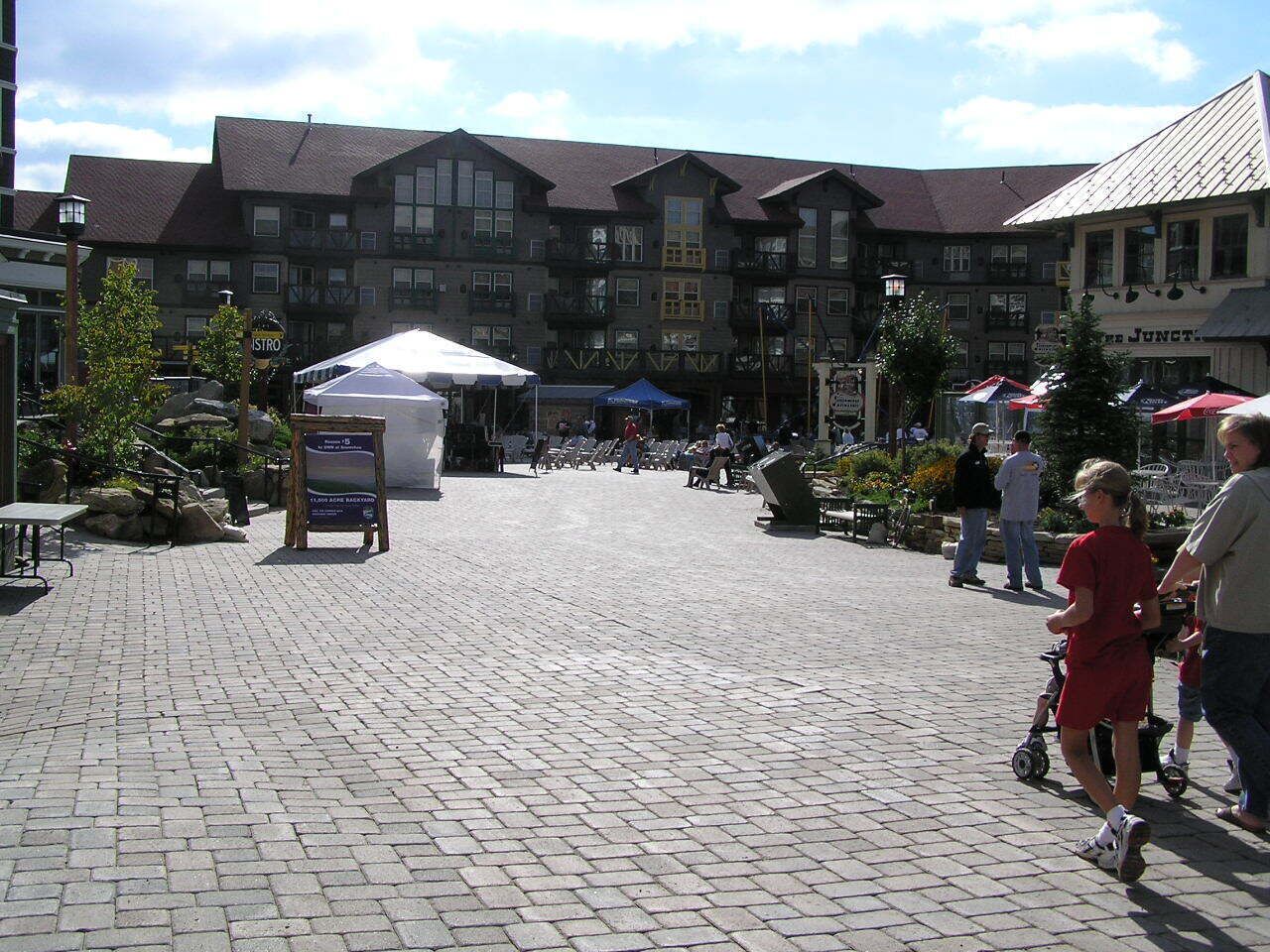 A cobblestone street with buildings, outdoor seating, and people walking.