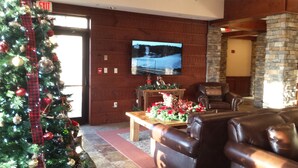 Eine gemütliche Lobby mit einem Weihnachtsbaum, Ledersofas, einem Kamin aus Stein und einem an der Wand montierten Fernseher.