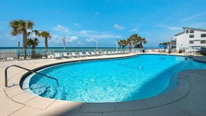 Ein Swimmingpool mit Liegestühlen und Palmen, mit Blick auf den Ozean.