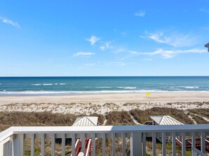 Blick auf einen Strand mit einer Holzterrasse, einer Flagge und einem Gebäude im Hintergrund.