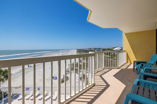 A balcony with a view of the beach, blue chairs, and sun loungers. - Stay @ Sandy Pause on Folly Beach (Folly Beach)