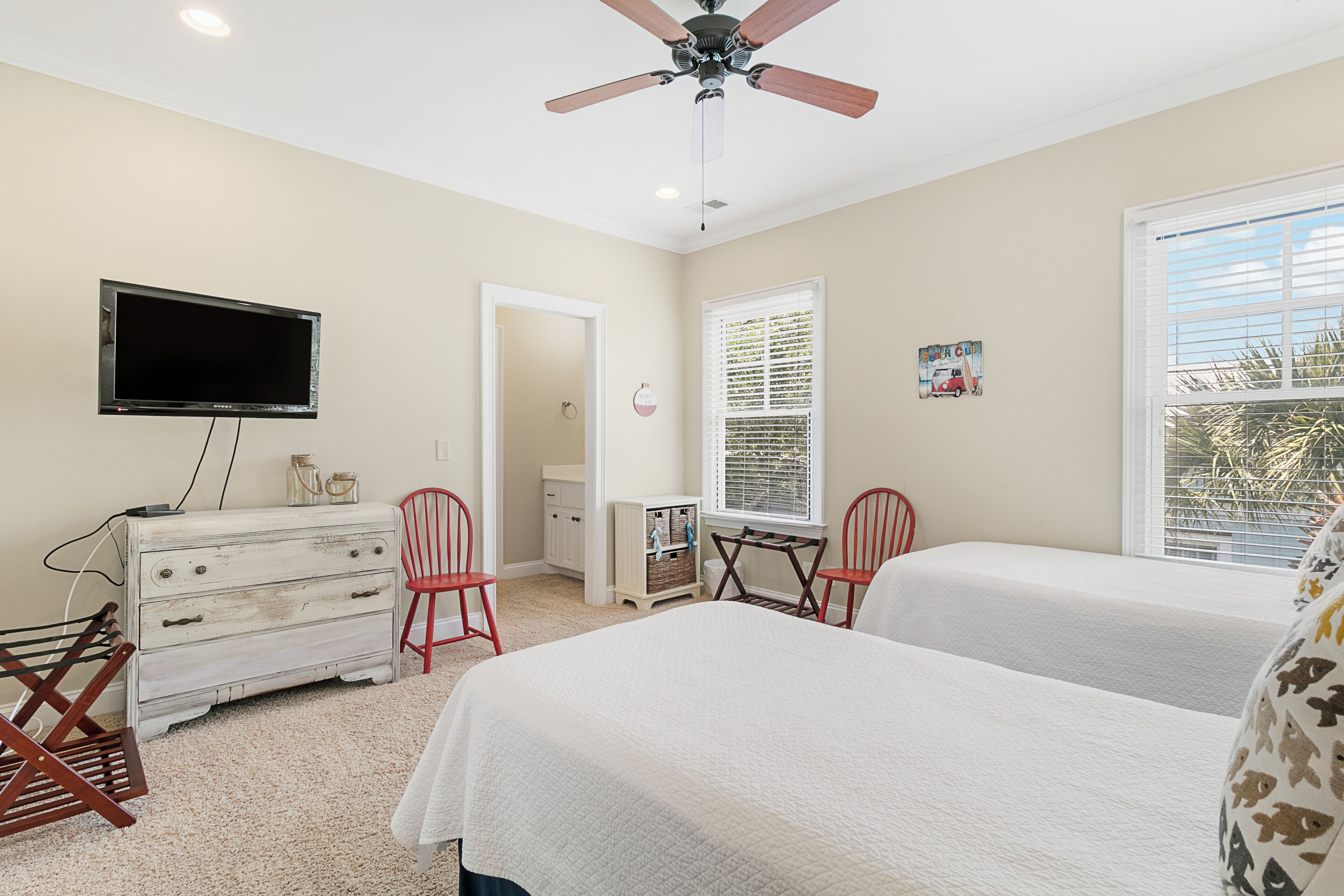 A bedroom with two beds, a ceiling fan, a television, and a window with blinds.