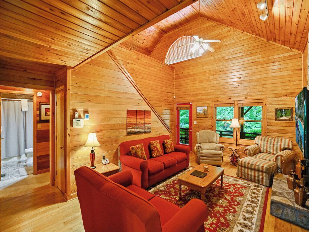 L’intérieur chaleureux d’un chalet, avec un revêtement mural en bois, un canapé rouge, une table basse et un fauteuil.