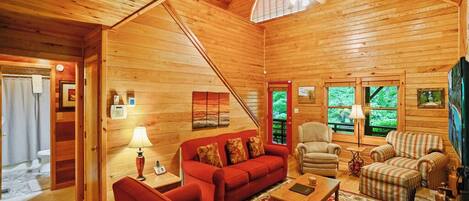 L’intérieur chaleureux d’un chalet, avec un revêtement mural en bois, un canapé rouge, une table basse et un fauteuil.
