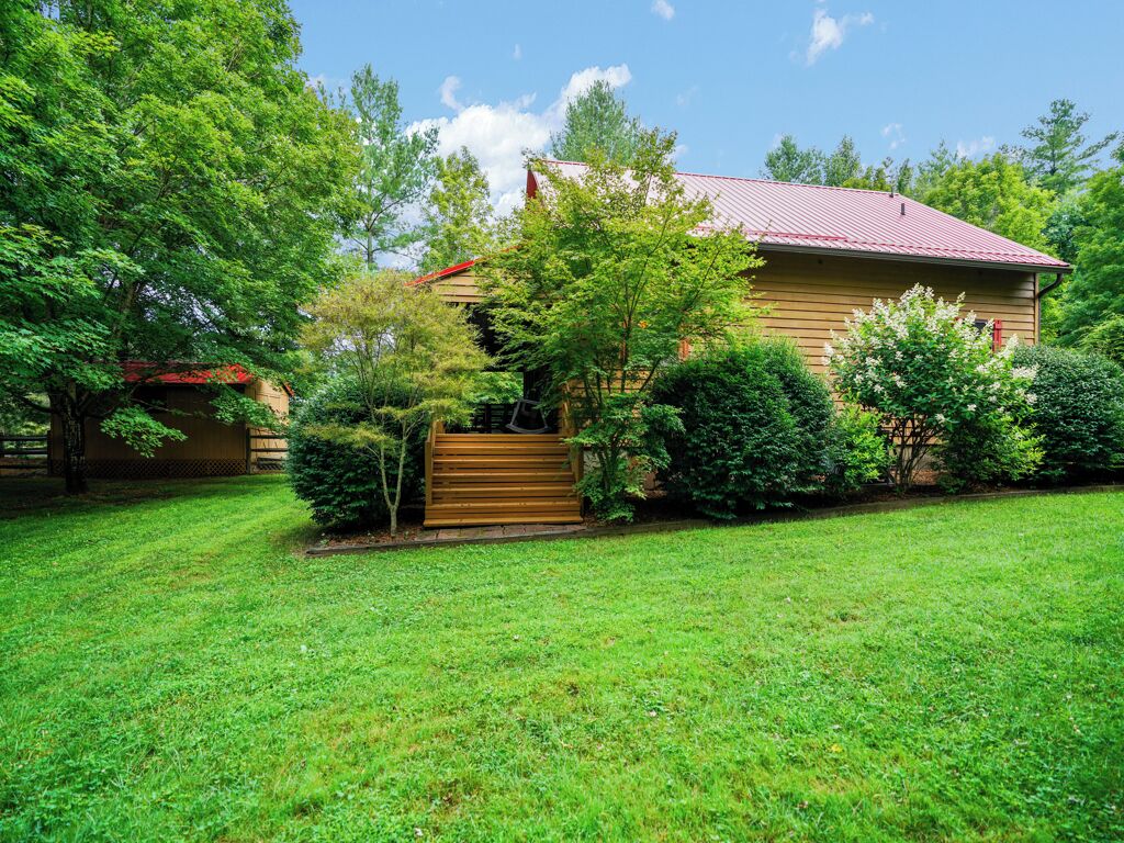 A single-story house with a red roof, surrounded by a well-maintained lawn and various shrubs.