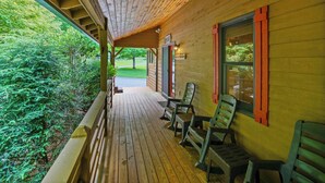 Un portico in legno con tetto spiovente, ringhiere di legno e tre sedie verdi.