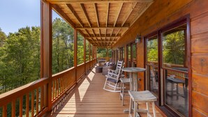 Une terrasse en bois avec des sièges extérieurs et de grandes fenêtres donnant sur une forêt.