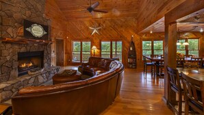 L’intérieur d’une cabane comprend une cheminée en pierre, un canapé en cuir, un coin repas et de grandes fenêtres.