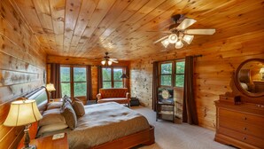 Une chambre dans une cabane en bois, comprenant un lit, deux chaises, un bureau, une commode et un ventilateur de plafond.