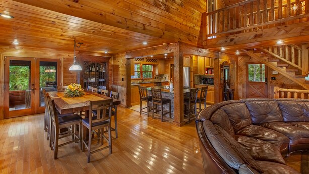 Un intérieur de chalet en bois spacieux, comprenant un coin repas, une cuisine et un grand canapé en cuir.