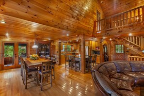 A spacious wooden cabin interior with a dining area, kitchen, and a large leather sofa.