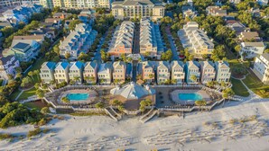 An aerial view of a resort with multiple buildings, a central pool, and a beach area with umbrellas. - Stay @ Serenity by the Sea on Isle of Palms (Isle of Palms)