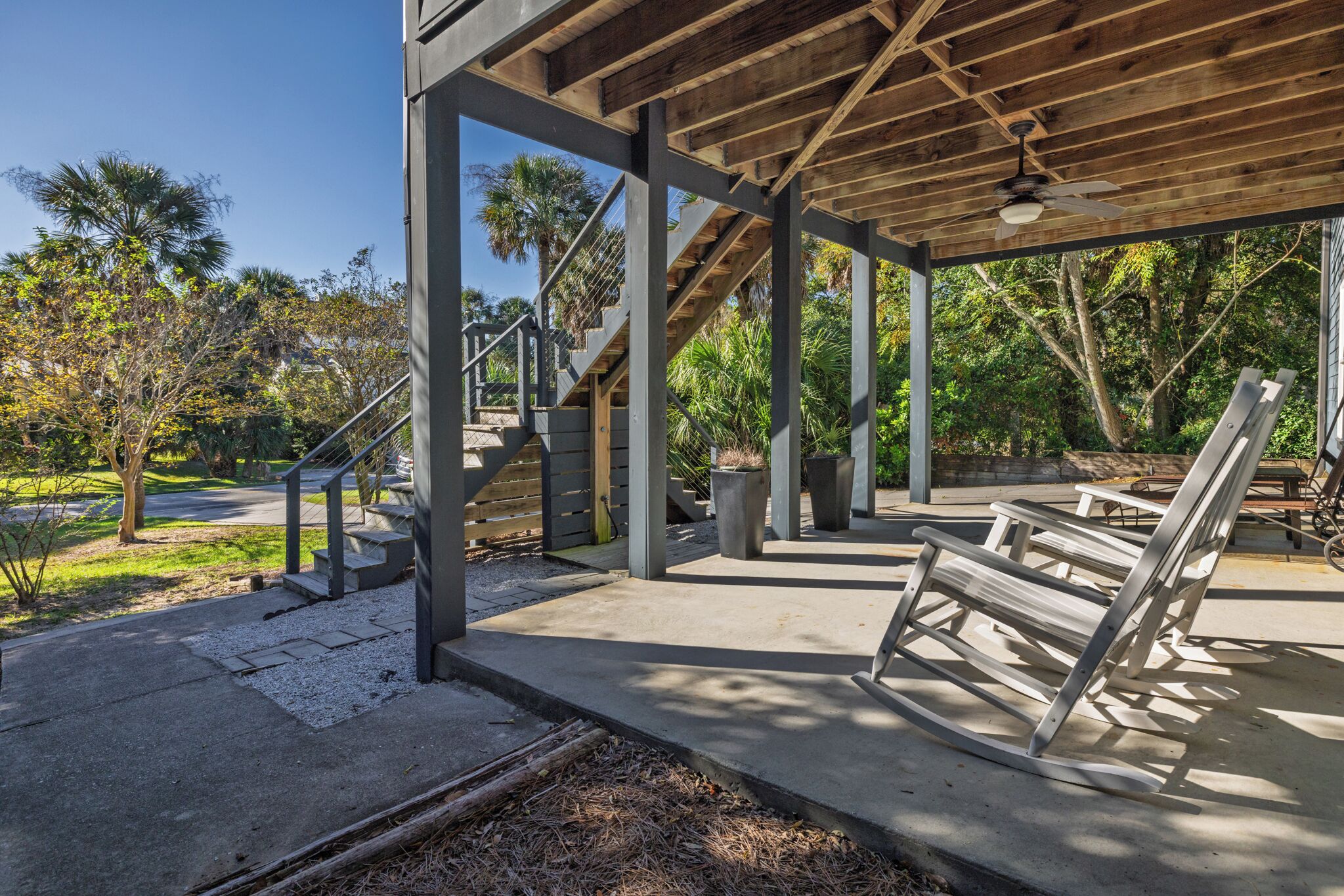 A covered outdoor area with concrete flooring, wooden benches, and a staircase leading to an upper level.