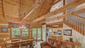 Ein geräumiges Wohnzimmer mit Holzboden, einem Ledersofa, einem Holzesstisch mit Stühlen und einem durch eine offene Tür sichtbaren Küchenbereich.