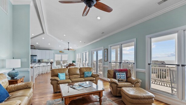 A spacious living room with a large window, a ceiling fan, and a view of the balcony. - 2nd Row Oceanview, private pool, elevator, golf cart, and easy beach access. (Emerald Isle)