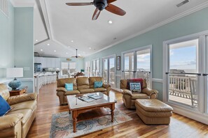 A spacious living room with a large window, a ceiling fan, and a view of the balcony. - 2nd Row Oceanview, private pool, elevator, golf cart, and easy beach access. (Emerald Isle)
