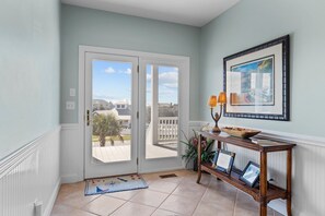 A hallway with a double door leading to a balcony, a console table with a lamp, and a framed picture on the wall.
